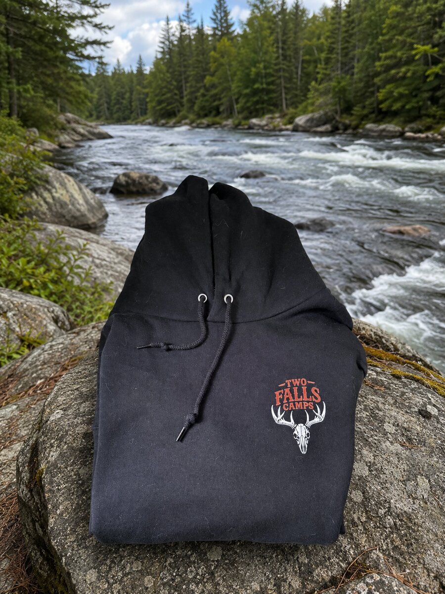 Trails End hoodie folded on a riverside rock, showing the Two Falls Camps skull logo